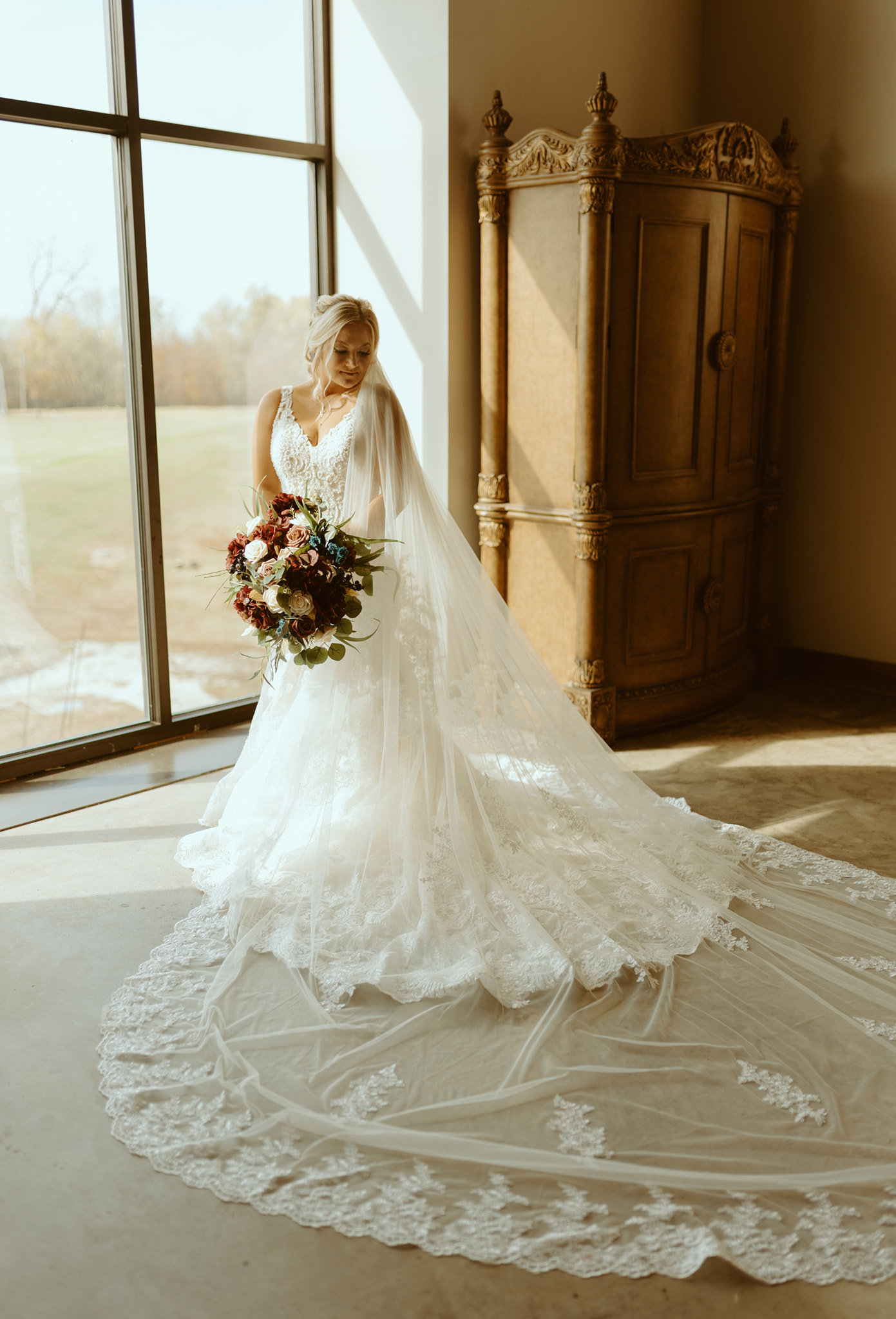 bride standing in large window in lace gown and long lace veil