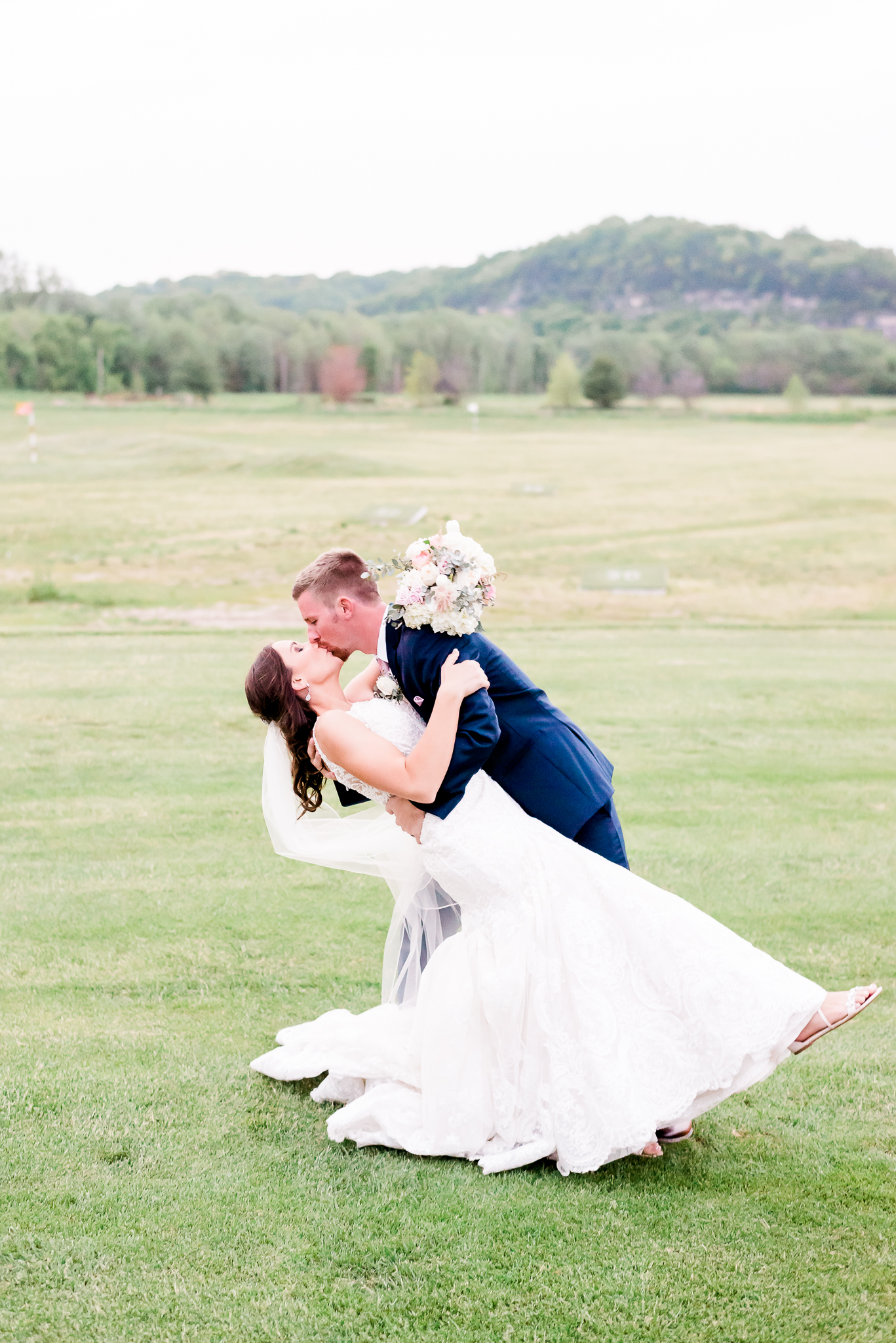 groom kissing bride in grassy field